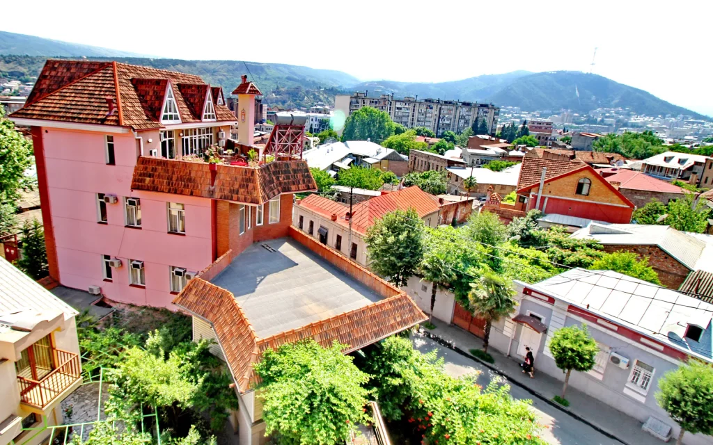 HOTEL IR-ME-NI — Aerial view of the pink hotel building and surrounding town with hills beyond.