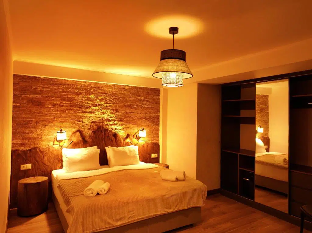 HOTEL USHBA — Cozy hotel bedroom with stone accent wall, double bed, and warm lighting.