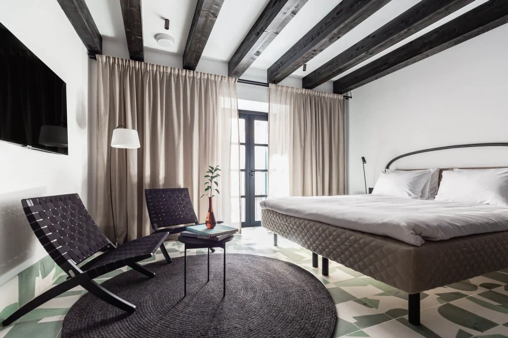 Hameau Mukhrani — Bedroom with exposed wood beams, king bed, and patterned tile flooring.