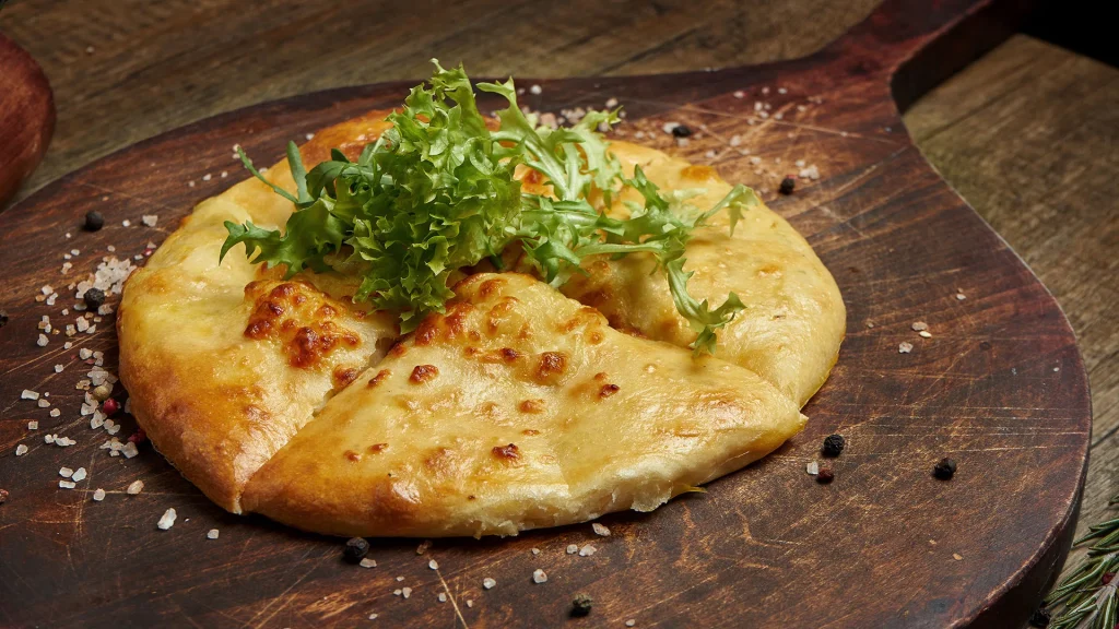Hotel Chiatureli — Cheese-filled bread served on a wooden board garnished with fresh greens.