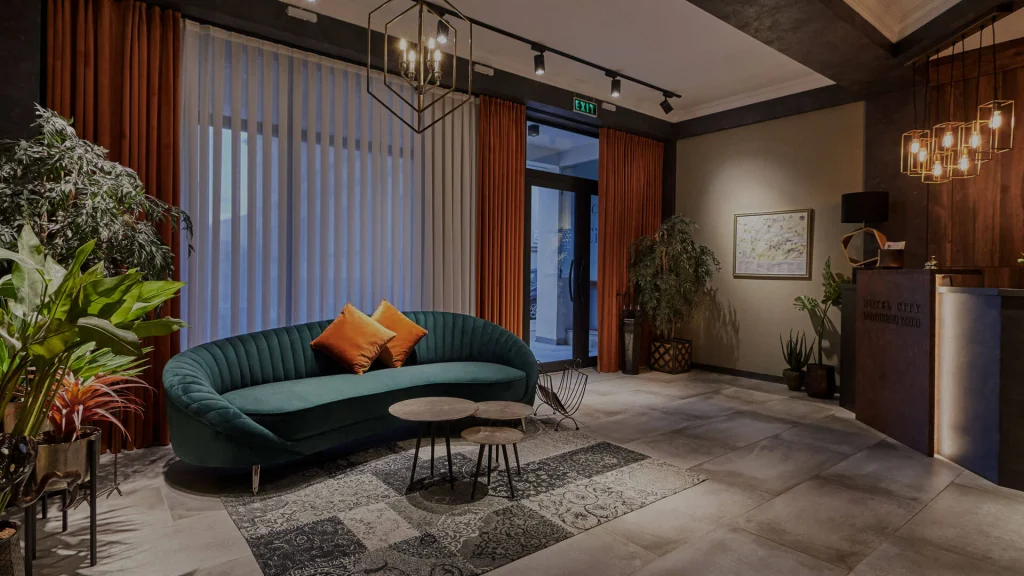Hotel City — Hotel lobby with teal velvet sofa, patterned rug, and warm pendant lighting.