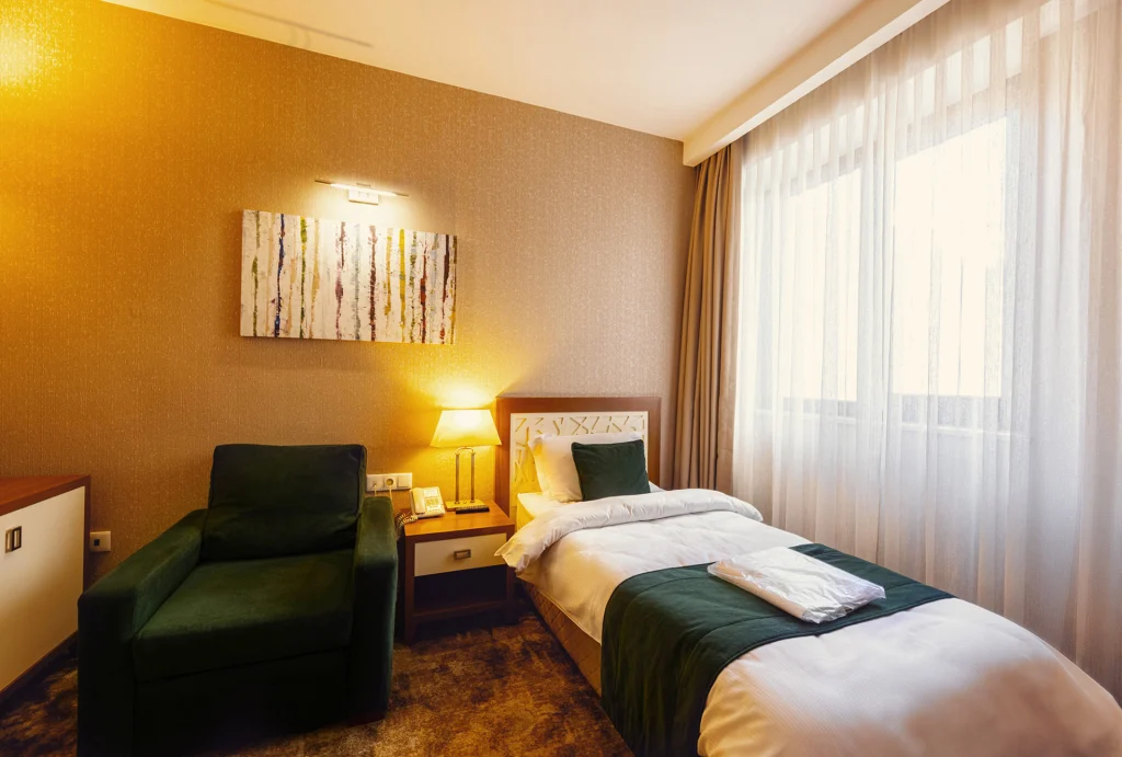 Hotel Costé — A cozy hotel room with a single bed, green armchair, and large window.
