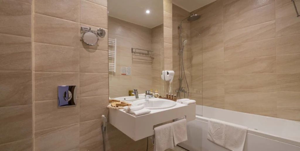 Hotel Costé — Modern bathroom with a bathtub, glass shower, and beige tile finishes.