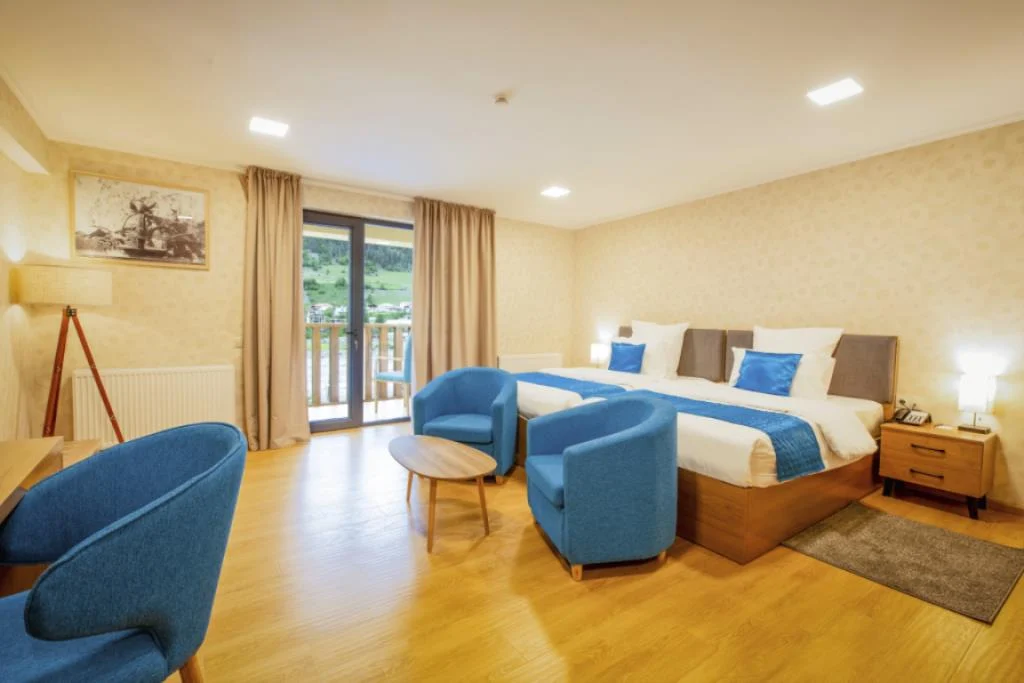 Hotel Gistola In Mestia — Spacious hotel room with twin armchairs, large bed, and balcony overlooking green valley.