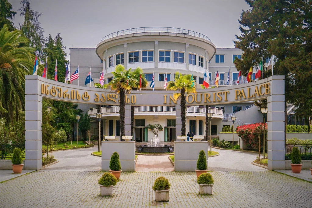 Hotel Intourist Palace — Hotel entrance archway with flags, palm trees, and a fountain leading to the main building.