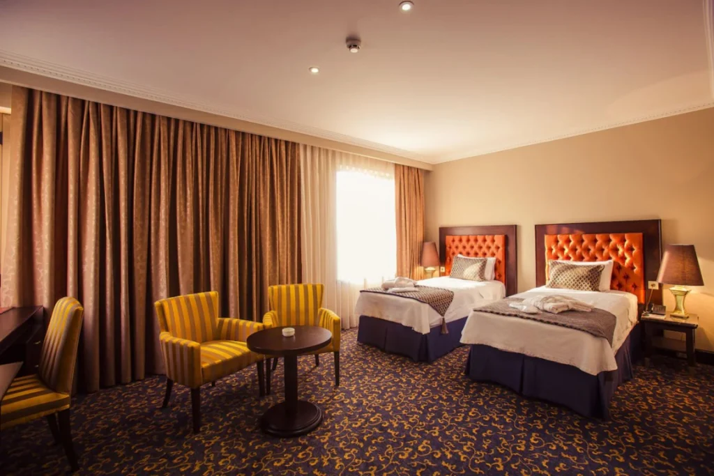 Hotel Intourist Palace — Twin bedroom with tufted orange headboards, striped armchairs, and patterned carpet.
