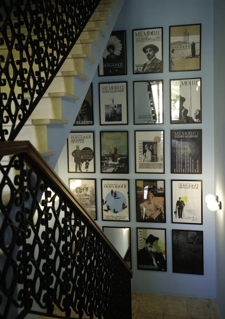 Hotel Memoire — Ornate staircase with wrought-iron railing beside a wall of framed artwork.