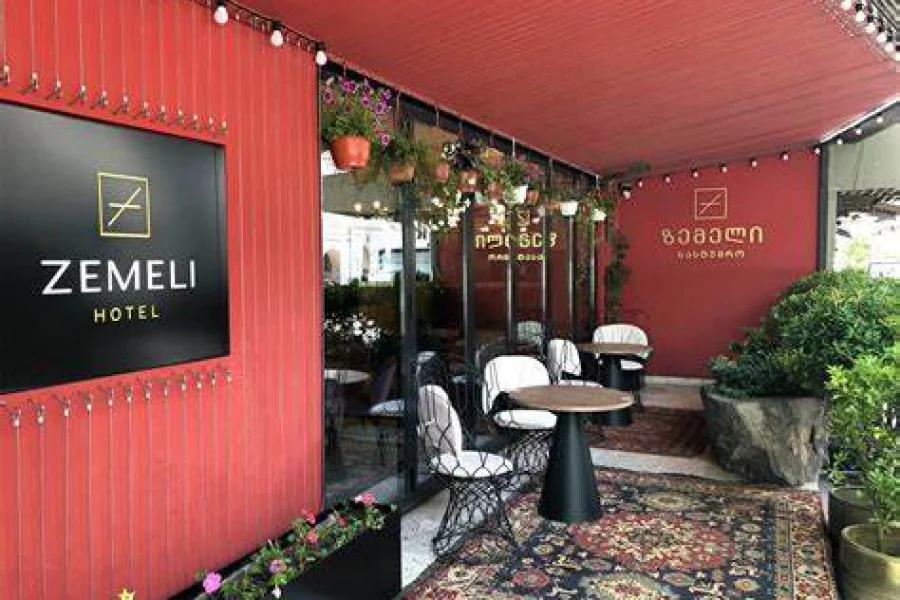 Hotel Zemeli — Hotel Zemeli entrance with red facade, outdoor café tables and hanging plants.