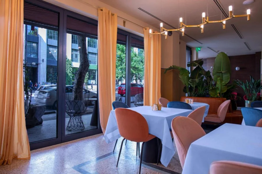 Hotel Zemeli — Hotel restaurant with set tables, velvet chairs and large windows facing the street.
