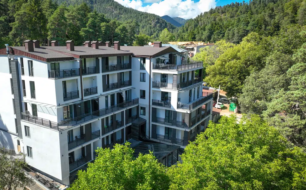 IFANI — Multi-story hotel building surrounded by forested mountains with balconies on each floor.