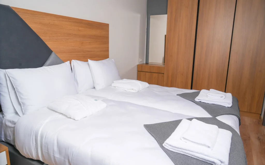 IFANI — Hotel bedroom with a neatly made bed, white linens, and folded towels.