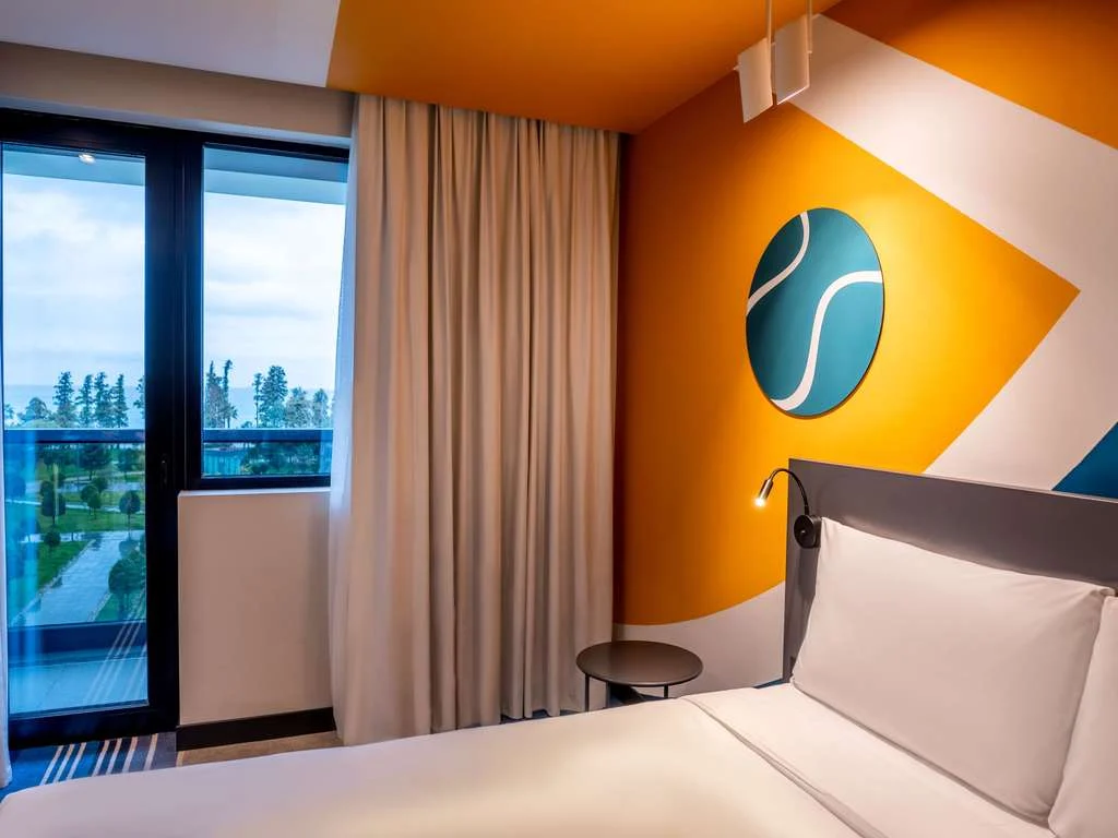 Ibis Styles Batumi — Colorful guest room with sea view balcony and sports-themed wall art.