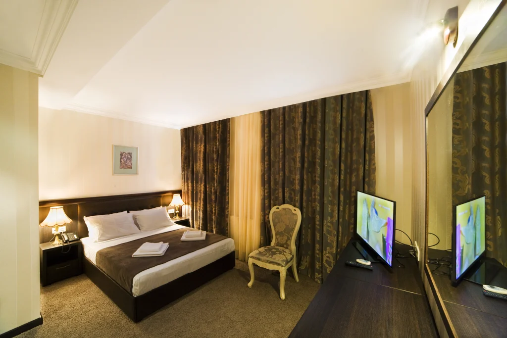 KALASI — Cozy hotel room with a dark wood bed, patterned curtains and television.