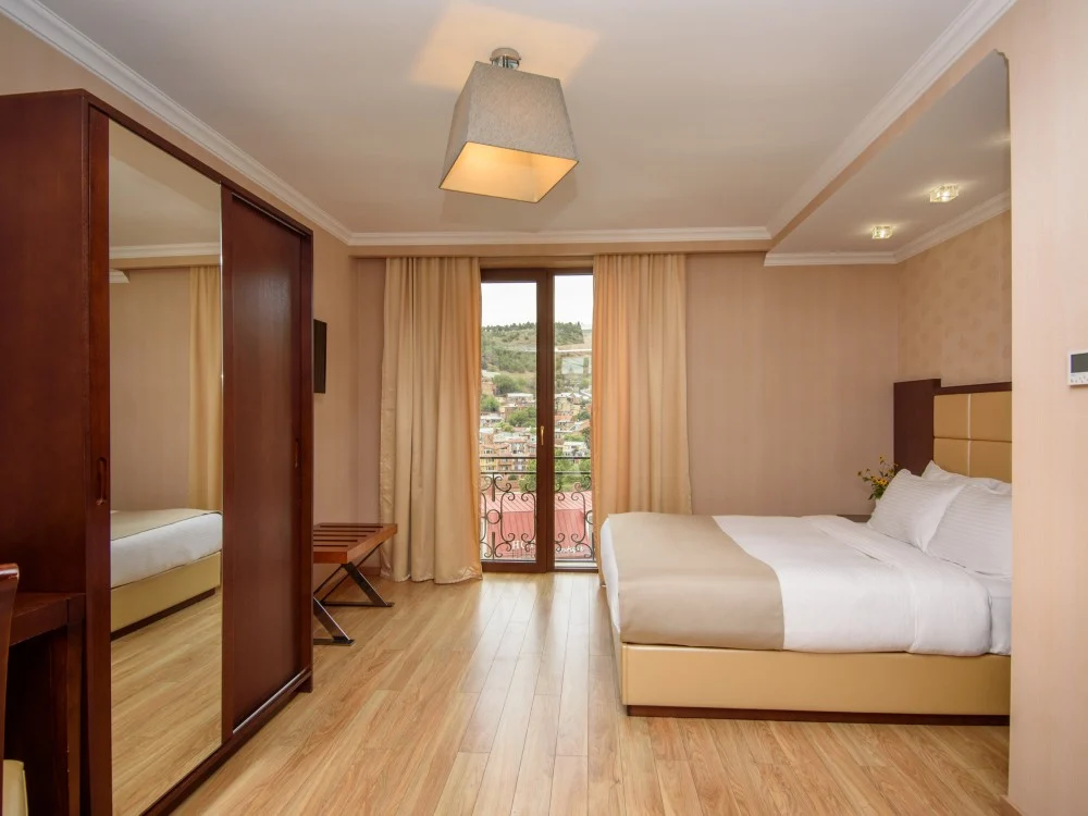 KMM Hotel — Bedroom with wooden floors, wardrobe, and a balcony overlooking the hillside town.