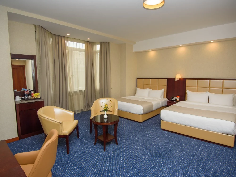 KMM Hotel — Spacious double room with two beds, seating area, and blue patterned carpet.