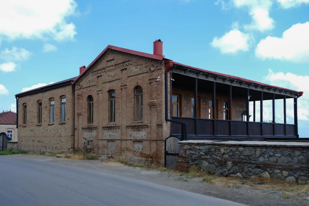 Kardanakhi Estate — Brick estate building with red roof, arched windows, and a covered wooden veranda.