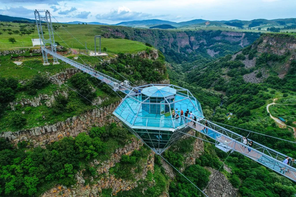 Kass Land Diamond Resort — Glass observation deck suspended over a dramatic green canyon with a suspension bridge.