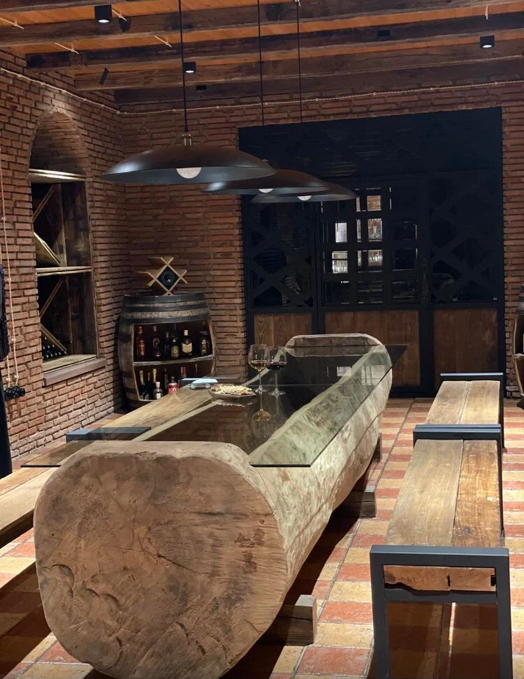 Kazbegi Cottages — Rustic wine cellar lounge with wooden benches and a glass-topped barrel table.