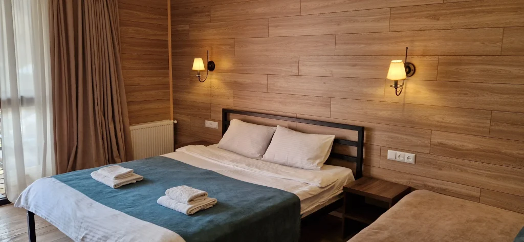 Kazbegi Cottages — Cozy wood-paneled guest room with a double bed and wall sconce lighting.