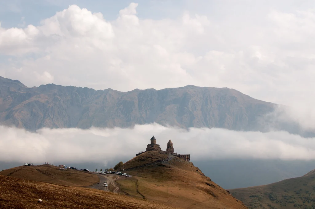 Kazbegi Cottages — Mountain view of a historic church perched on a hilltop above the clouds.
