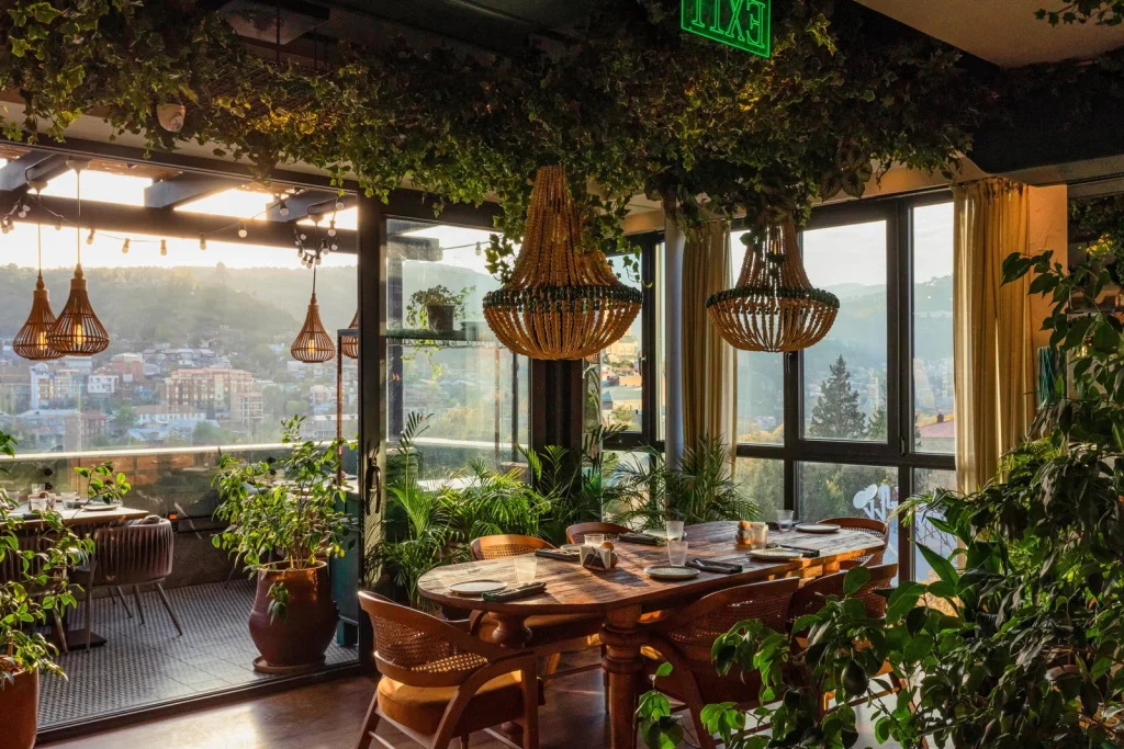 Khedi — Rooftop restaurant terrace with greenery, chandeliers, and a scenic hillside town view.