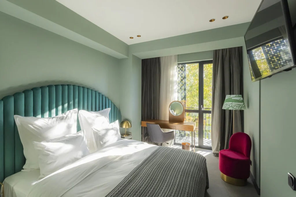Khedi — Hotel room with teal tufted headboard, white bedding, and balcony with curtains.