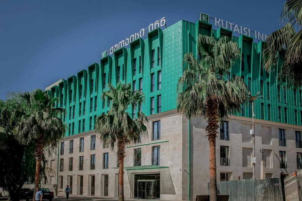 Kutaisi Inn — Modern multi-story hotel building with green glass facade and palm trees out front.