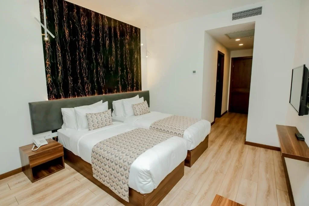 Kutaisi Inn — Twin bed guest room with wooden flooring and dark patterned headboard wall.