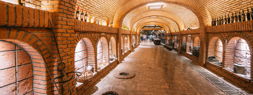 Kvareli Wine Cave — Brick vaulted wine cave corridor lined with arched storage niches and bottles.
