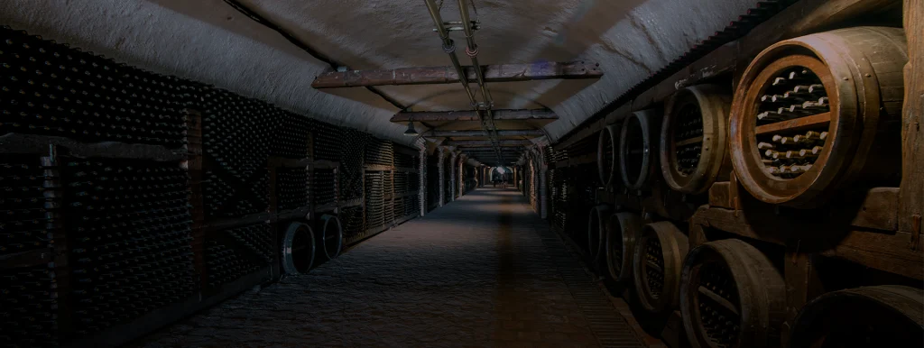 Kvareli Wine Cave — Dim underground cellar tunnel with aging barrels and bottle racks along the walls.