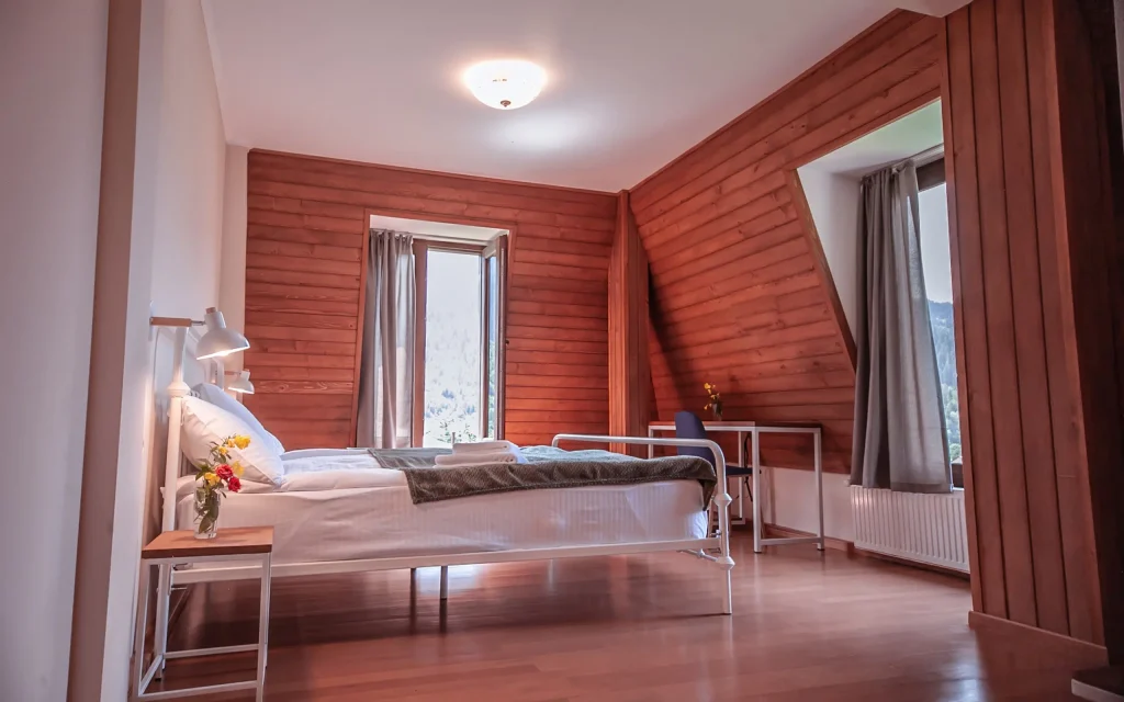 Latour mestia — Attic-style bedroom with wood-paneled walls, a double bed, and a window view.