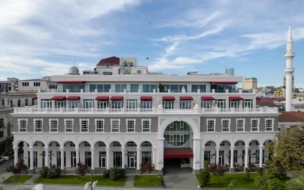 Le Port Boutique Apart Hotel — Elegant white building facade with arched entrance, red awnings and rooftop terrace.