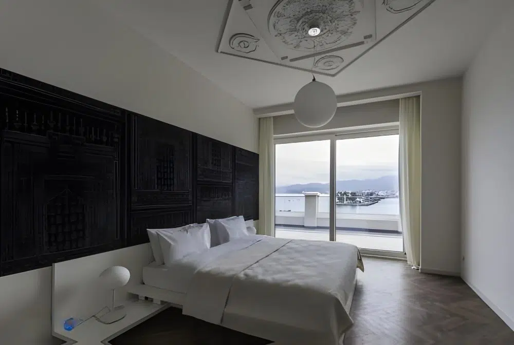 Le Port Boutique Apart Hotel — Bedroom with decorative ceiling and floor-to-ceiling window overlooking the sea and coastline.