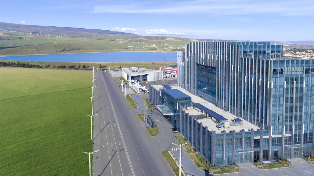 Legends Bar — Aerial view of the modern glass hotel building beside a lake and green fields.