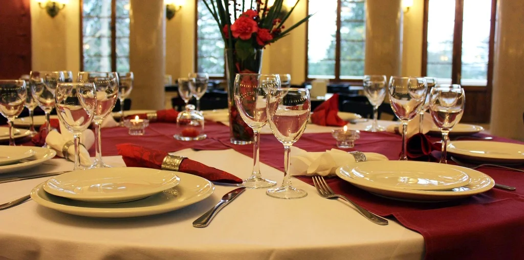 Legends Tskaltubo Spa Resort — Elegantly set dining table with wine glasses, white plates, and red linens.