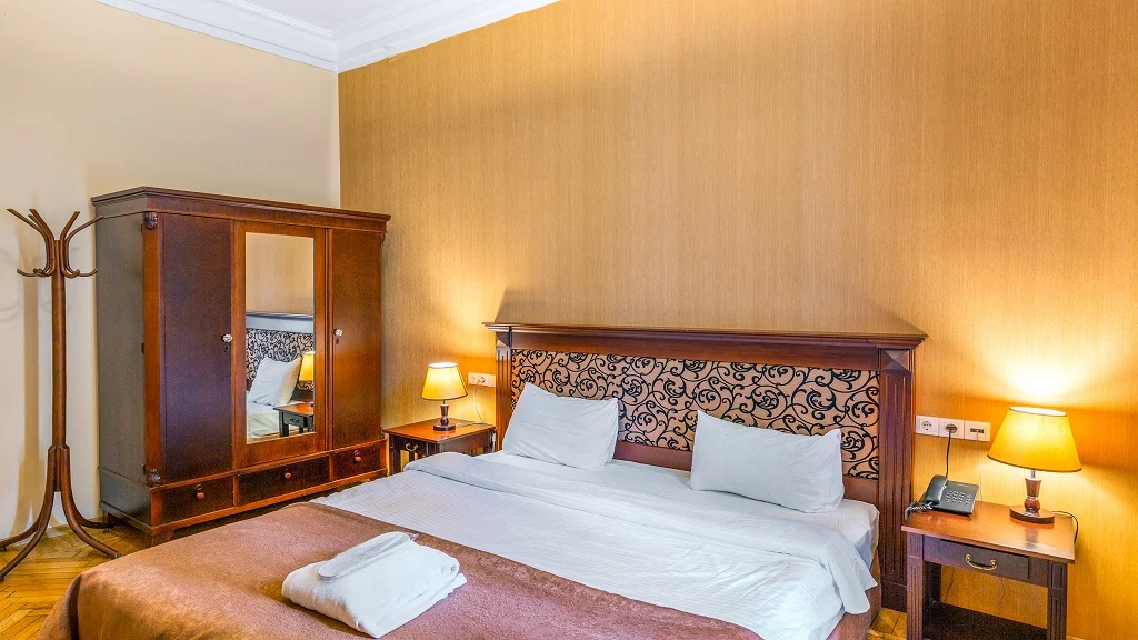 Legends Tskaltubo Spa Resort — Hotel room with a double bed, wooden wardrobe, and bedside lamps.