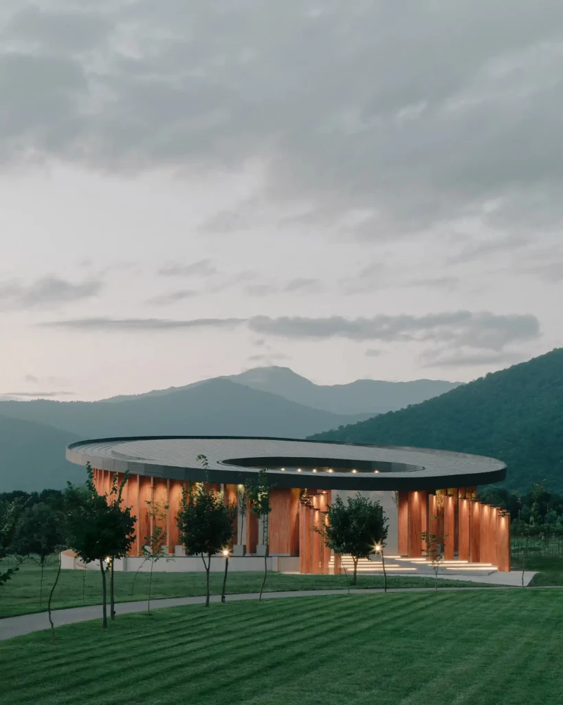 Lopota Lake Resort & Spa — Modern circular building with wooden slats set against mountain scenery at dusk.