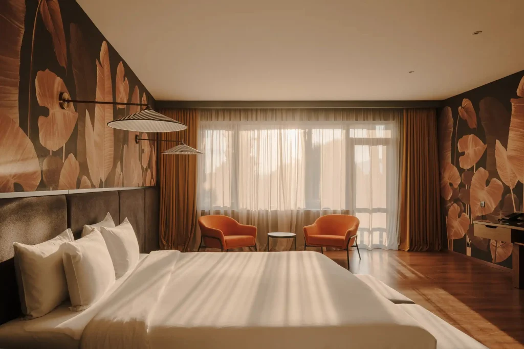 Lopota Lake Resort & Spa — Spacious hotel room with a large bed, orange armchairs, and botanical wall mural.