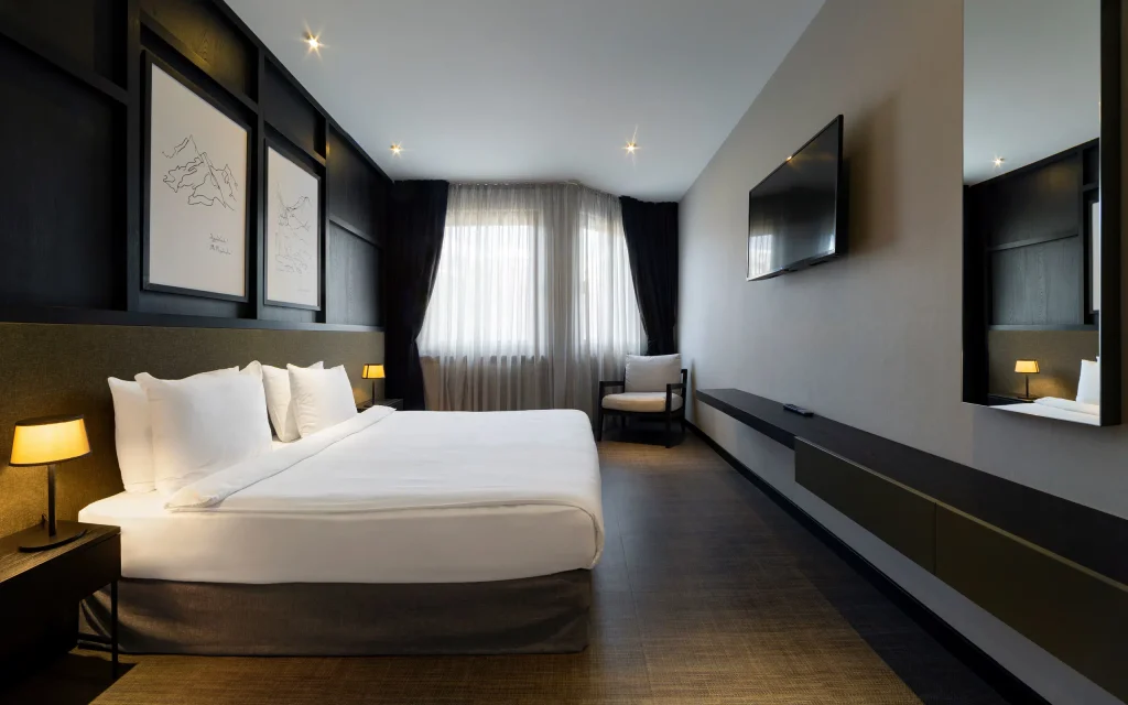 Marco Polo Hotel Gudauri — Modern hotel bedroom with a large bed, dark decor, and wall-mounted television.