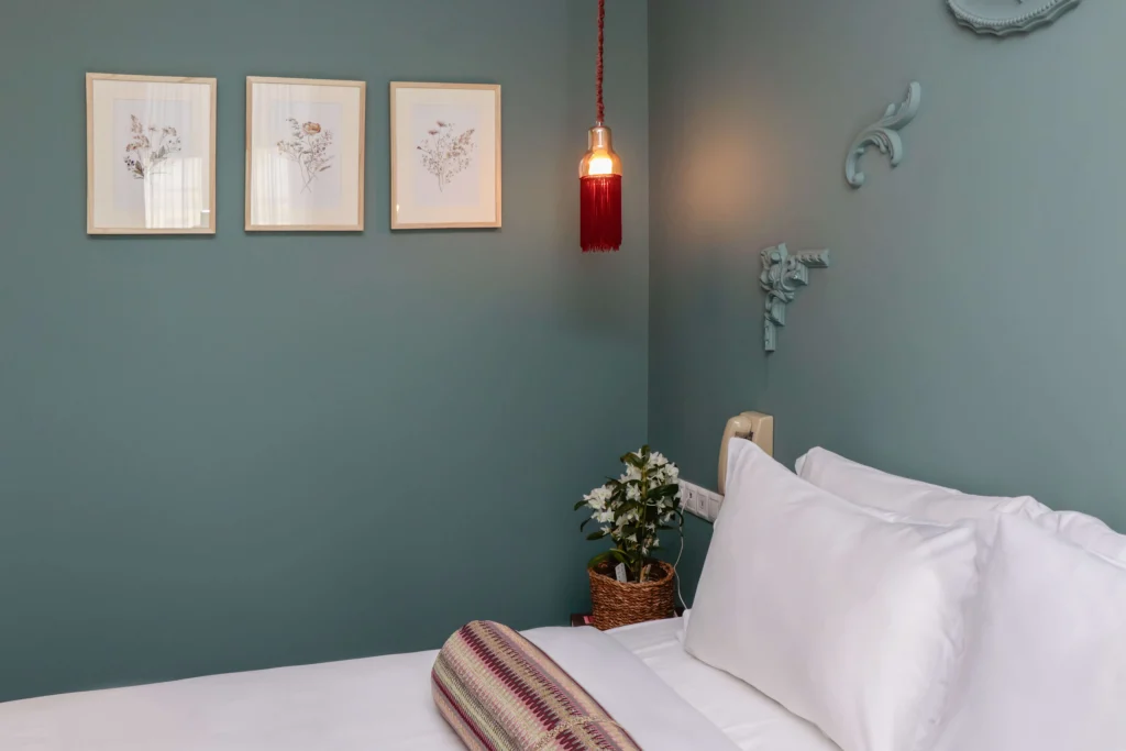 Margot Old Tbilisi — Bedroom corner with teal walls, botanical prints, and a red pendant light beside the bed.