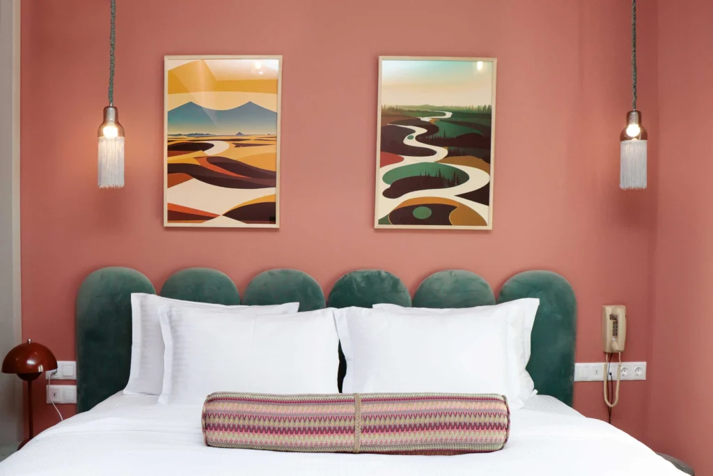 Margot Old Tbilisi — Bedroom with green upholstered headboard, coral walls, and framed landscape artwork above the bed.