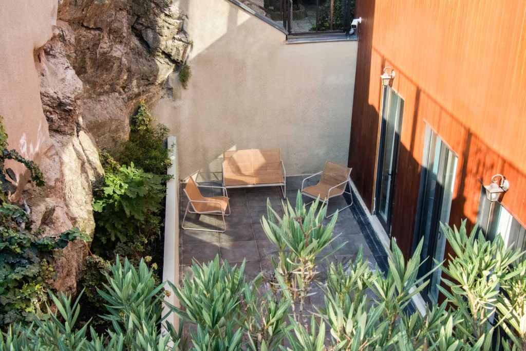 Margot Sololaki — Outdoor terrace with seating tucked against a natural rock face and greenery.