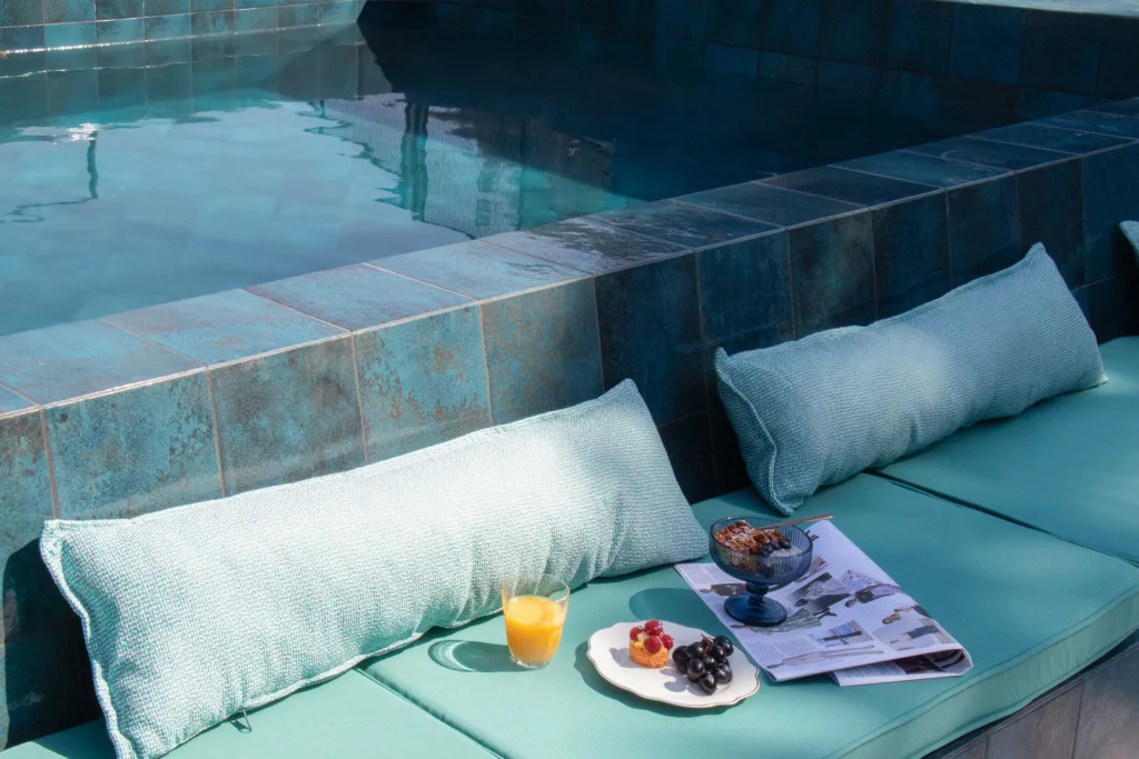 Margot Sololaki — Poolside lounge area with teal cushions, fresh fruit, and a drink served poolside.