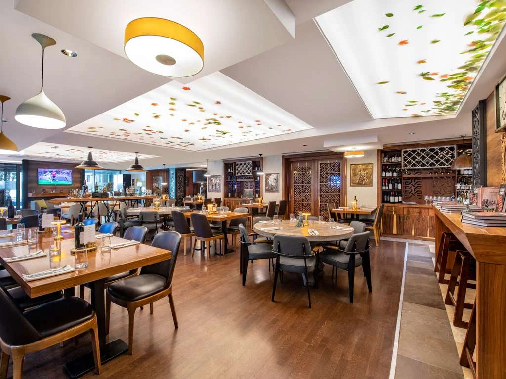 Mercure Tbilisi Old Town — Hotel restaurant with wooden tables, patterned ceiling panels, and a well-stocked wine display.