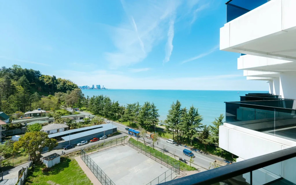 Mziuri Gardens — Elevated balcony view overlooking the coastline, sea, and distant city skyline.