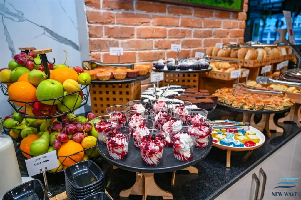 NEW WAVE HOTEL — Breakfast buffet spread with fresh fruit, pastries, and desserts on display.
