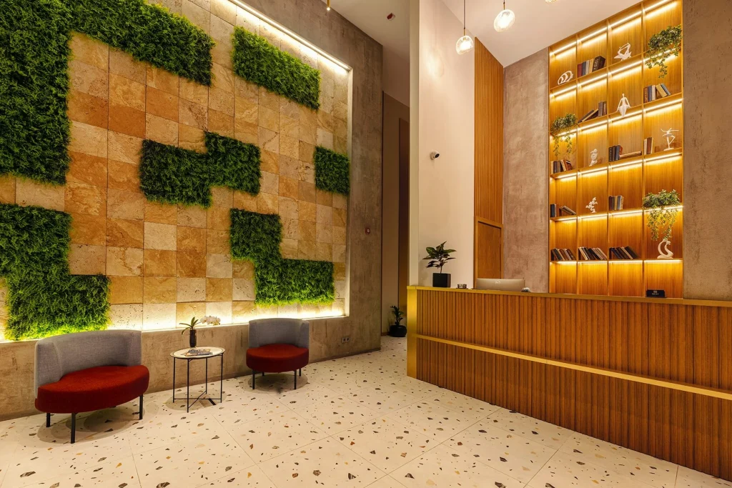 NEXT Apartments — Hotel lobby with reception desk, decorative shelving, and a green moss feature wall.