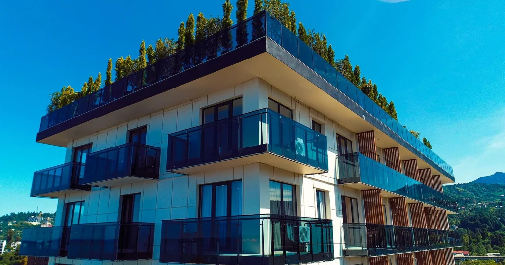 Next Green — Modern multi-story building with glass balconies and a rooftop garden under a clear blue sky.