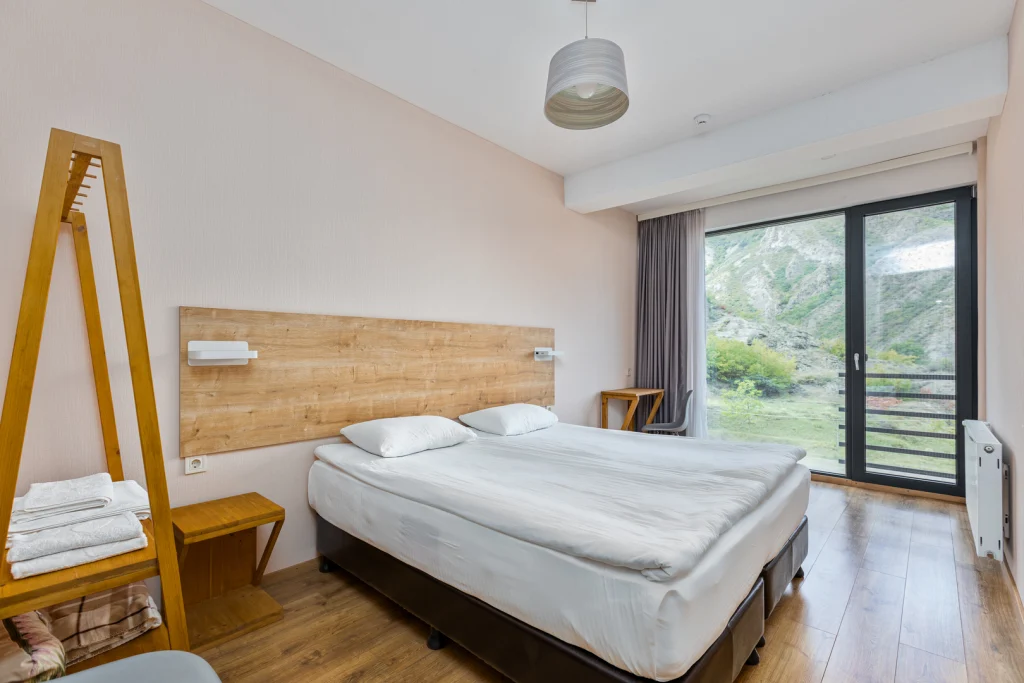 Nika Vacheishvili's Wine Cellar — Bright hotel bedroom with large bed and balcony view of mountains.