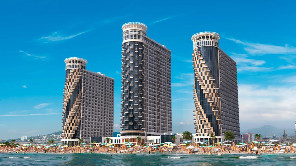 Orbi Beach Tower Hotel — Three modern beachfront towers rise above a crowded sandy beach under blue sky.